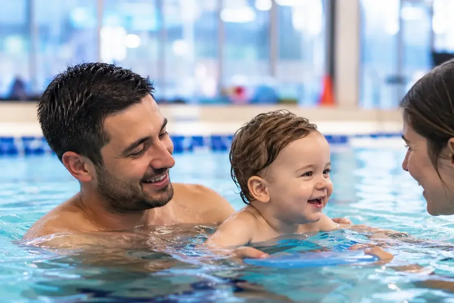Un papà accompagna il proprio bambino a pelo d’acqua durante una lezione genitore-bambino in vasca coperta — Genitore-bebè (1-2 anni)