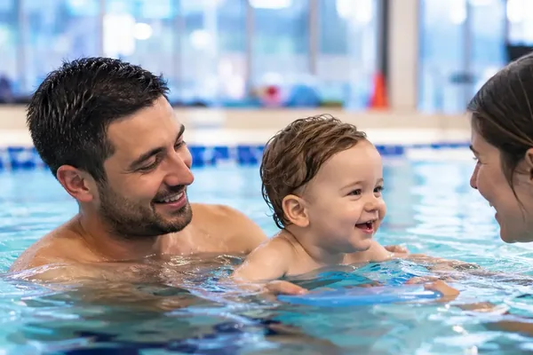 Un papà accompagna il proprio bambino a pelo d’acqua durante una lezione genitore-bambino in vasca coperta — Genitore-bebè (1-2 anni)