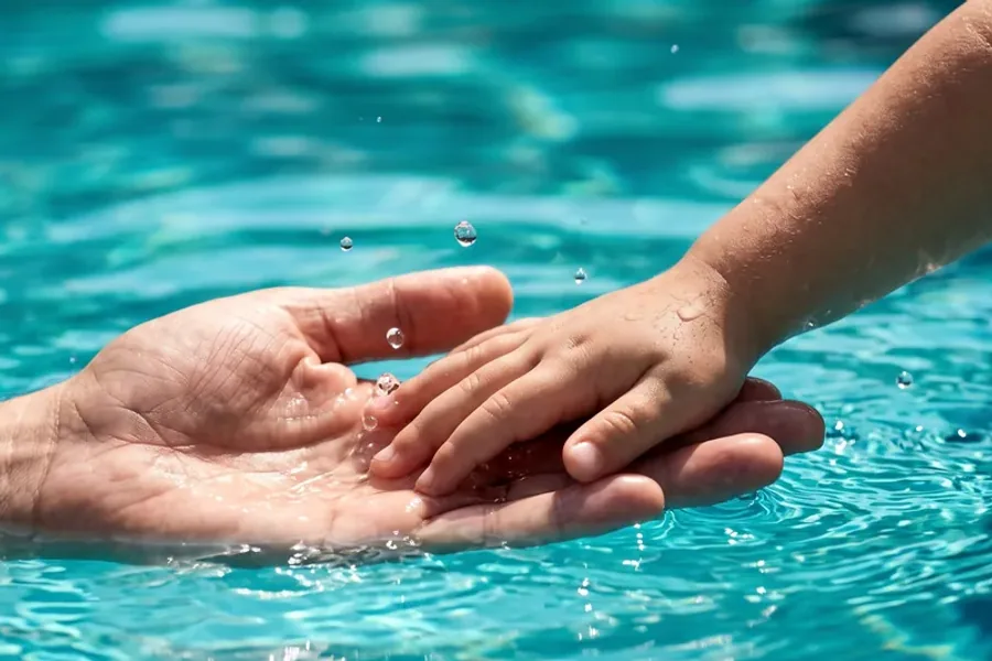 La mano di un adulto e quella di un bambino si sfiorano a pelo dell’acqua calda di una vasca Ondarte